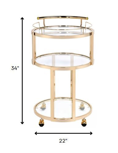 Elegant gold and clear glass serving cart with three shelves and caster wheels, perfect for serving meals and drinks.