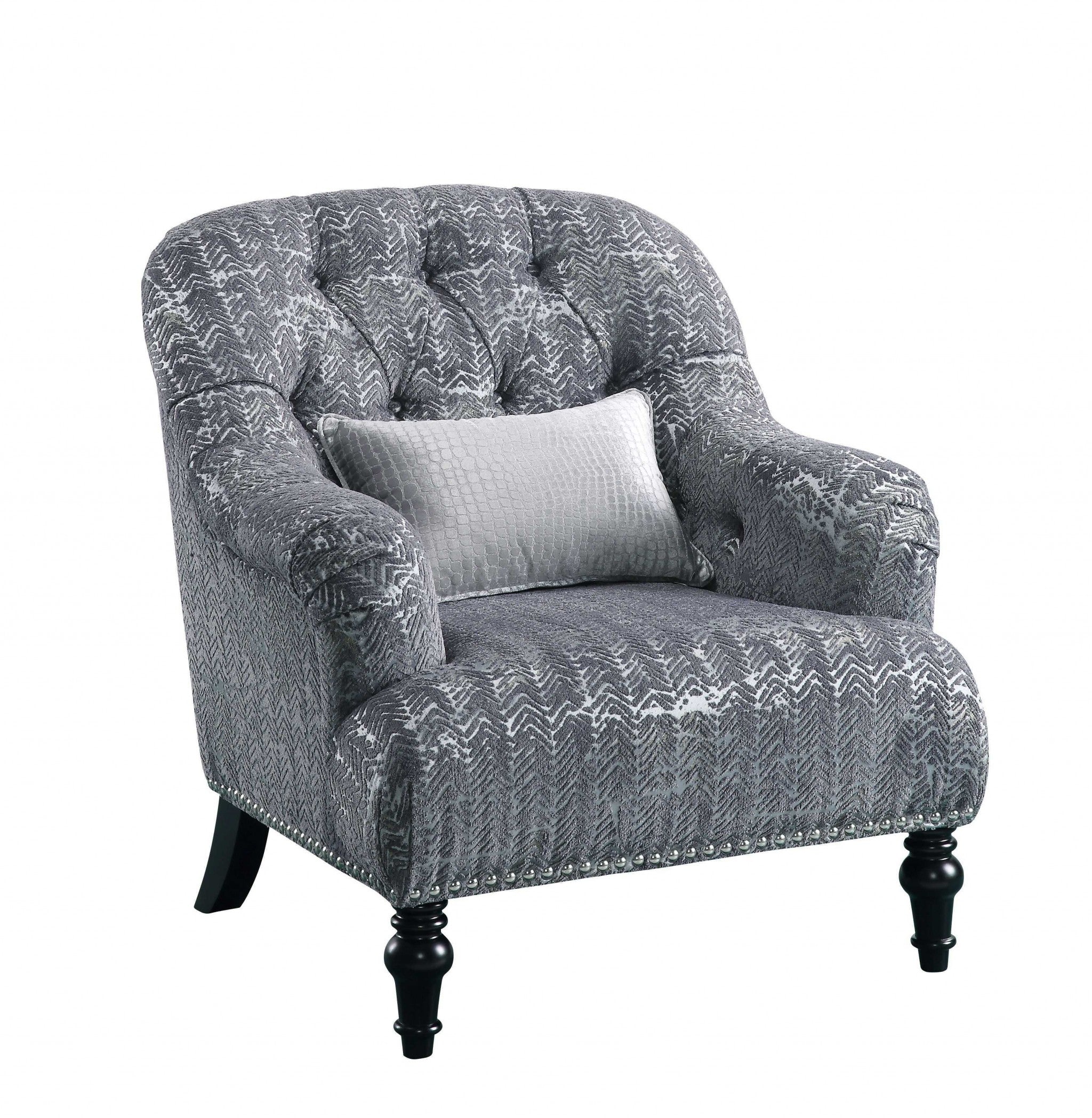 A stylish gray patterned velvet chair with a plush pillow, featuring button tufted back and arms, resting on black wood bun-turned legs.