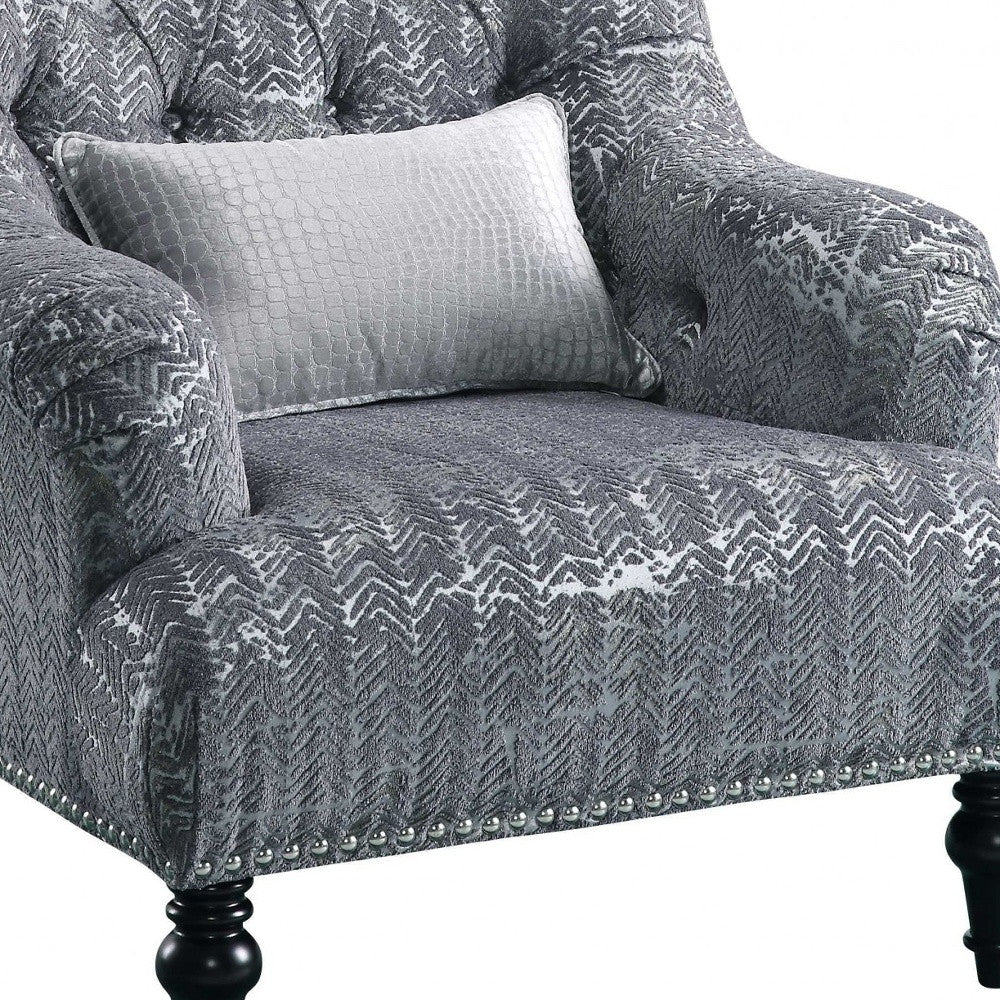 A stylish gray patterned velvet chair with a plush pillow, featuring button tufted back and arms, resting on black wood bun-turned legs.