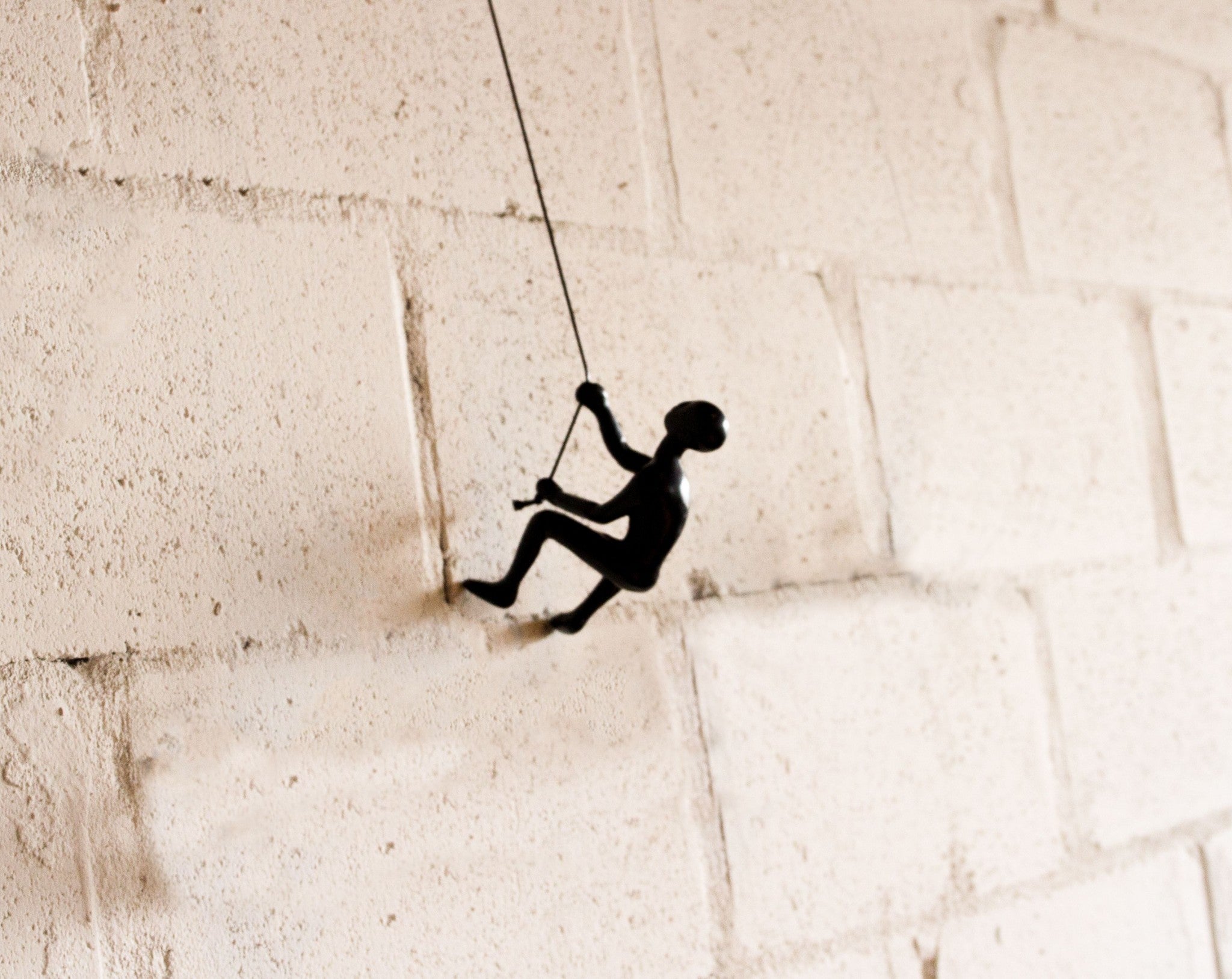 Black climbing man wall art sculpture made of solid resin, featuring a man climbing a rope with a leather hanging rope.