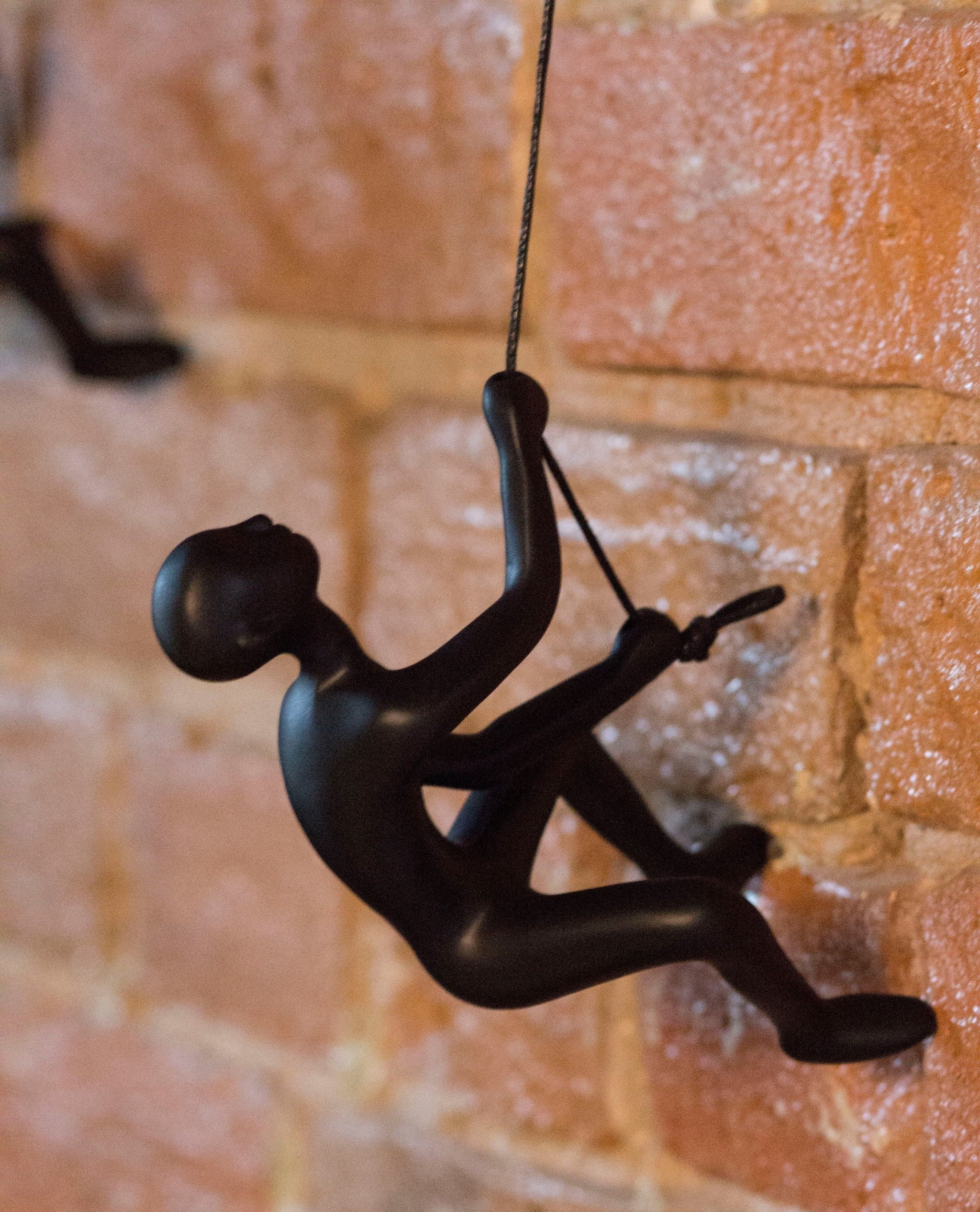 Black climbing man wall art sculpture made of solid resin, featuring a man climbing a rope with a leather hanging rope.