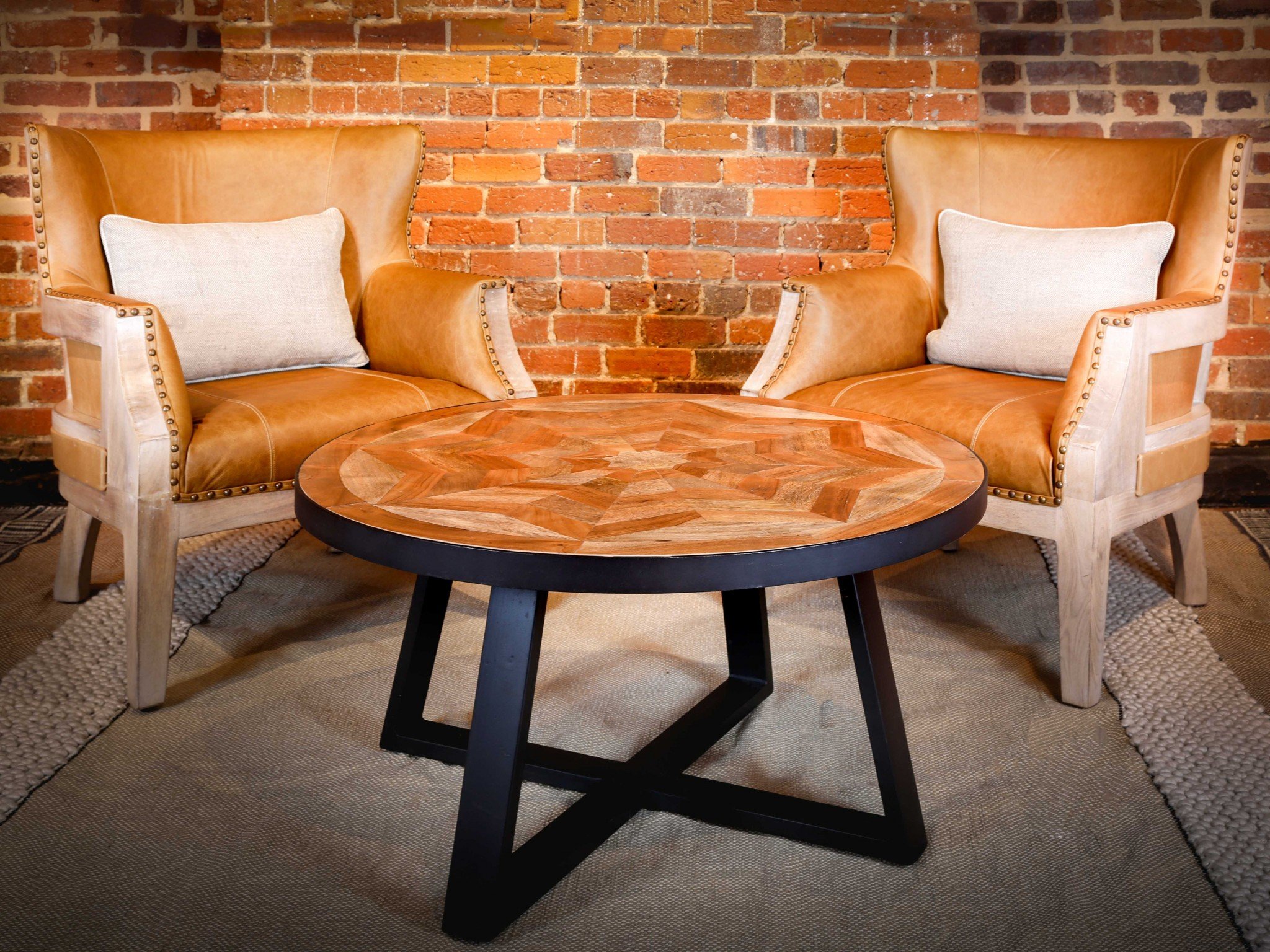 A stylish 36" x 36" coffee table featuring a concentric star inlay design made of acacia and mango wood, supported by a black metal criss-cross base.