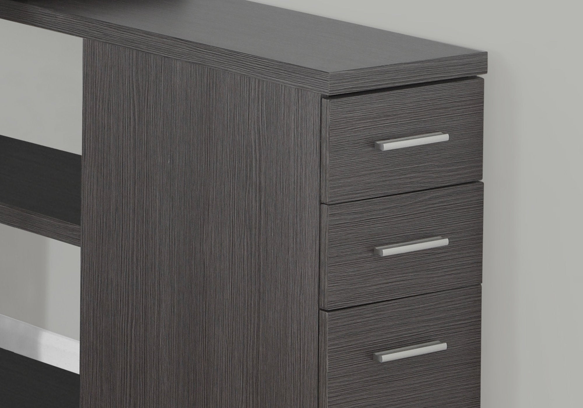 L-shaped computer desk in grey and silver particle board with three drawers and two shelves, perfect for office or home use.