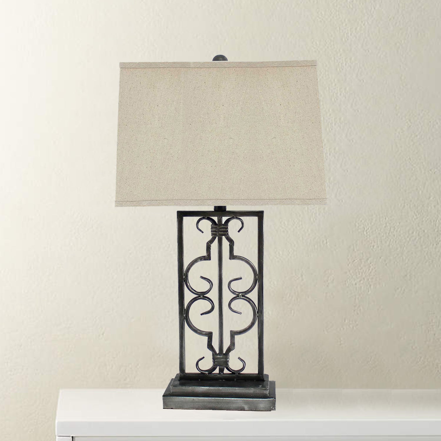 Gray industrial table lamp with stacked metal pedestal and beige linen shade, illuminating a stylish living space.