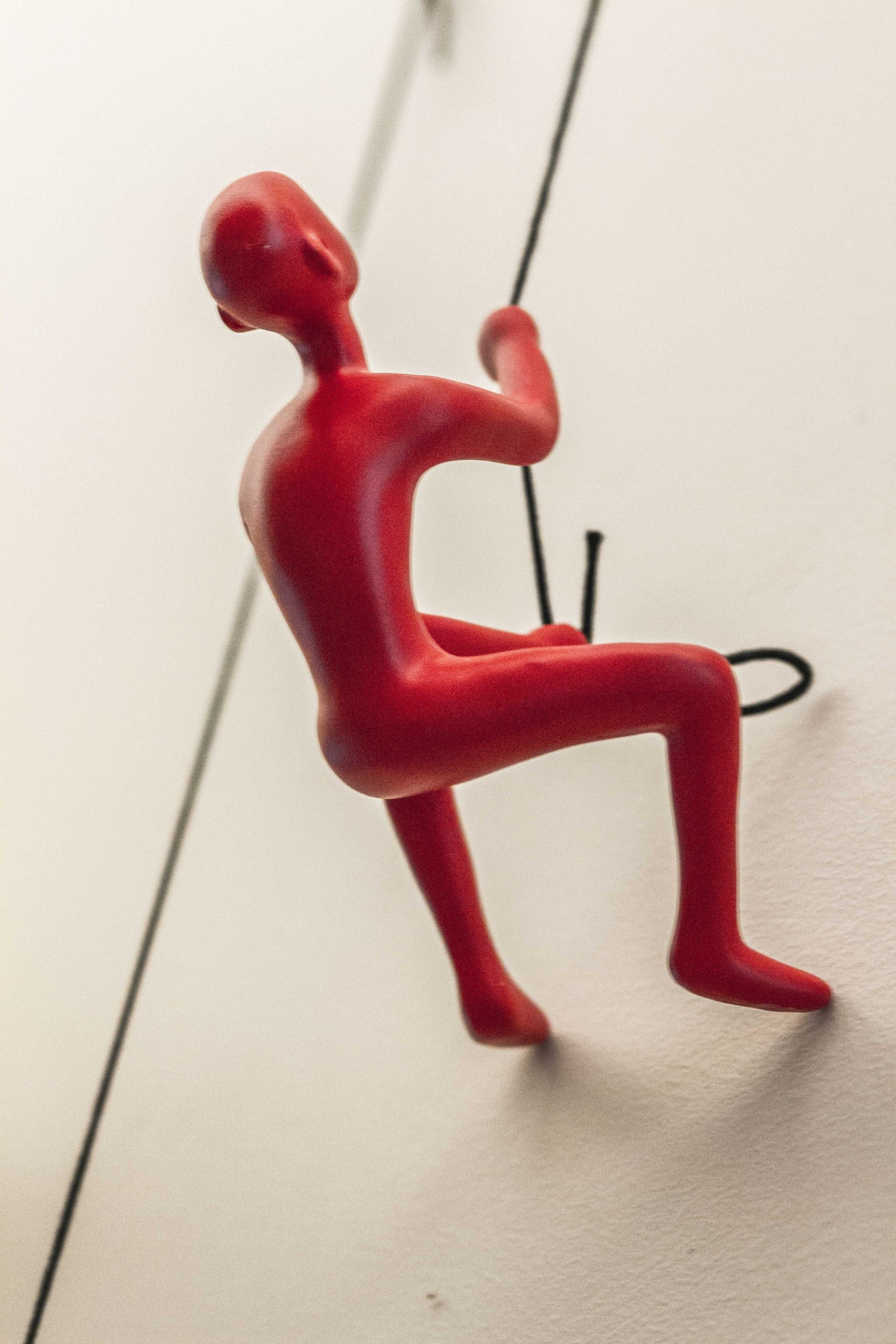 A vibrant red resin sculpture of a man climbing, showcasing a unique three-dimensional design for wall decor.