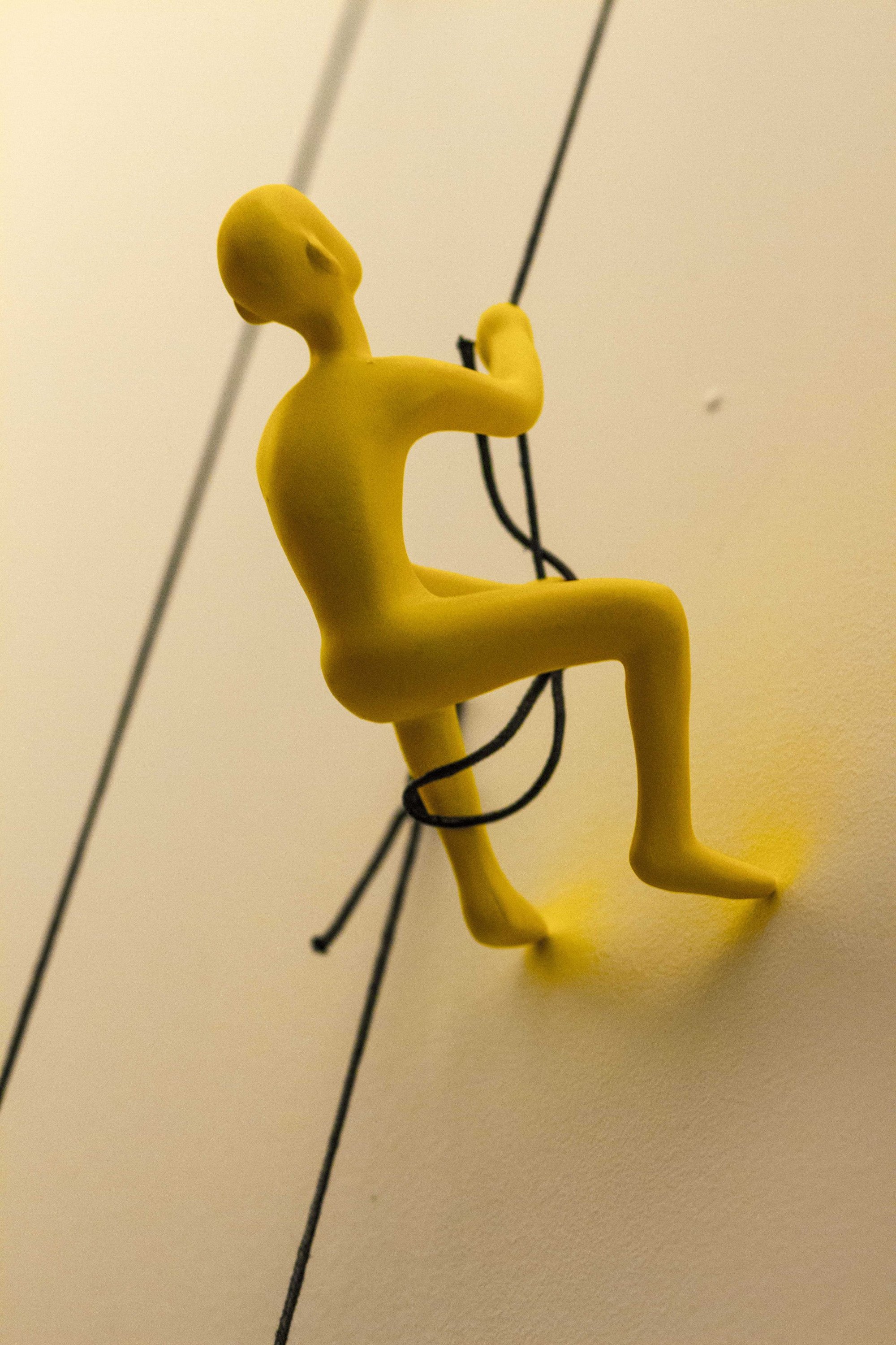 A vibrant yellow resin sculpture of a man climbing, designed for wall art decoration, showcasing a modern and unique aesthetic.