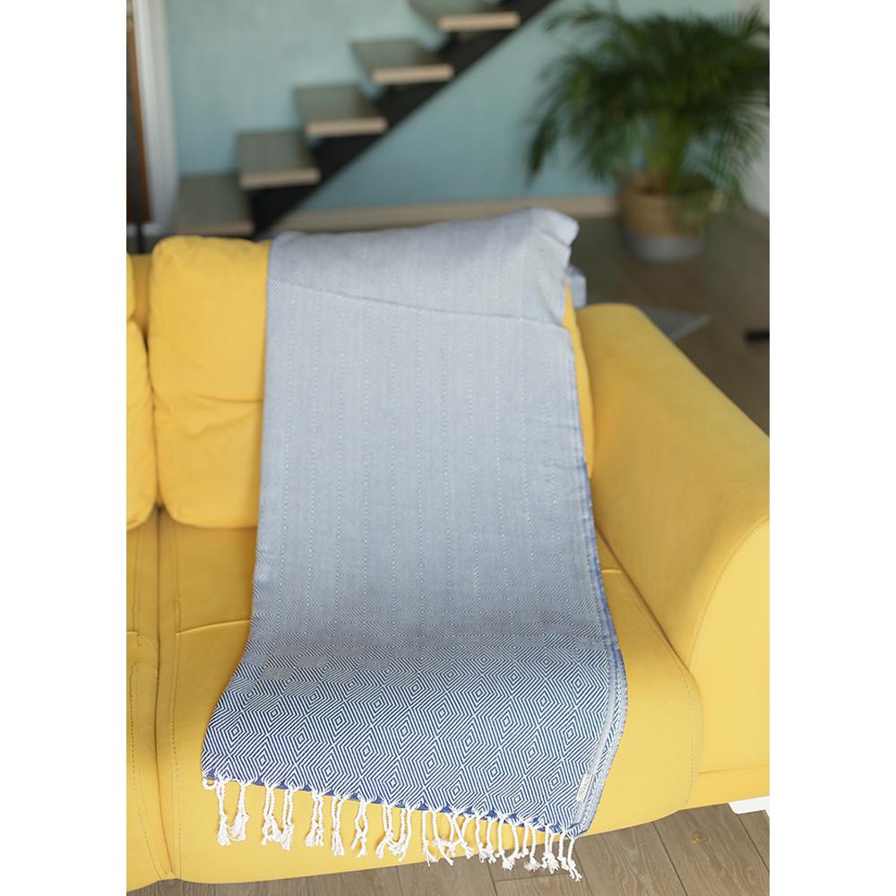 A 70-inch blue geometric handwoven throw blanket displayed elegantly on a couch, showcasing its intricate patterns and high-quality cotton material.