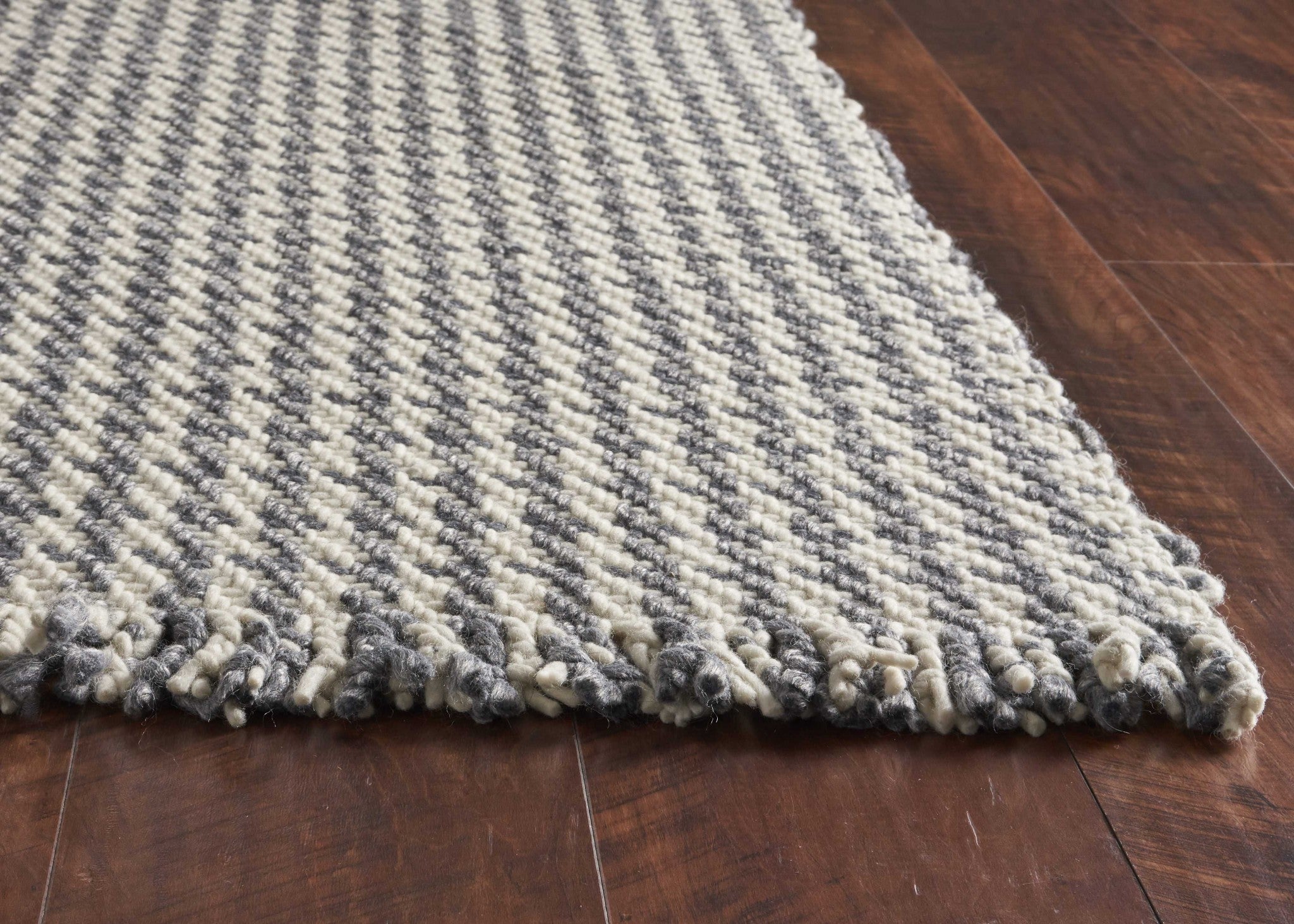 A luxurious 7x9 inches wool area rug in ivory and grey houndstooth pattern, featuring braided fringe for a modern touch.