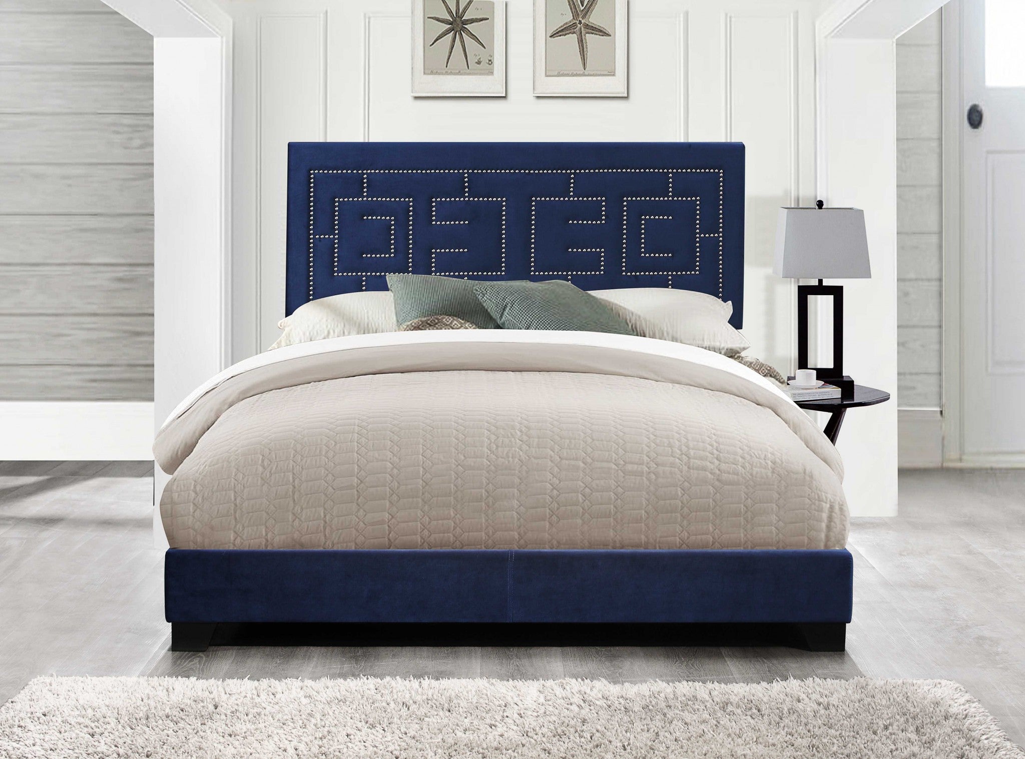 A luxurious dark blue velvet upholstered bed with a padded headboard and low-profile footboard, featuring chrome nailhead trim.