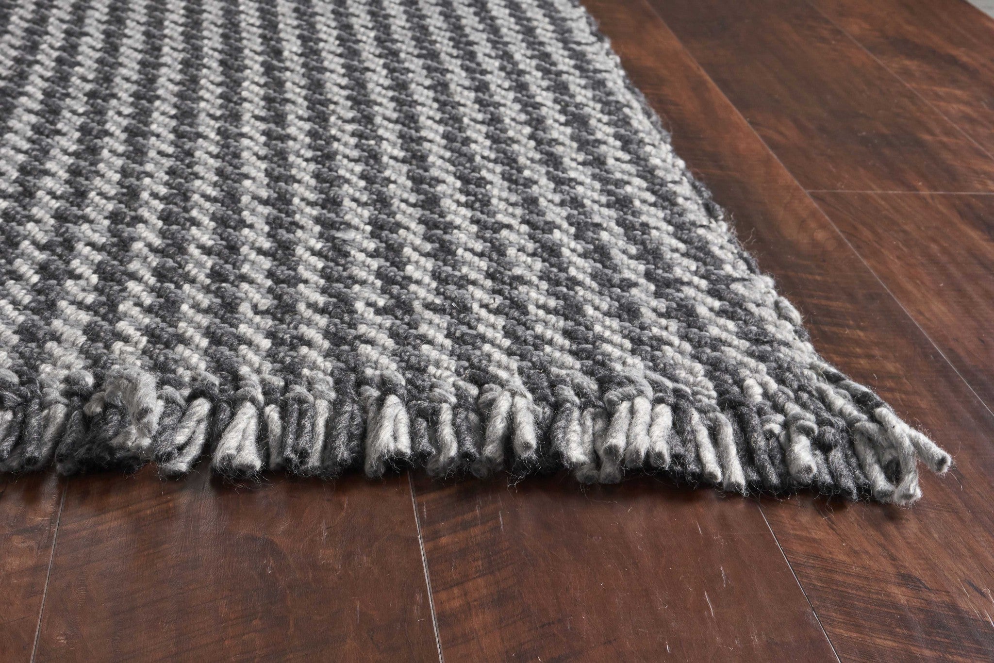 A beautifully crafted 8x10 grey hand woven houndstooth indoor area rug featuring a modern design and braided fringe, perfect for enhancing home decor.