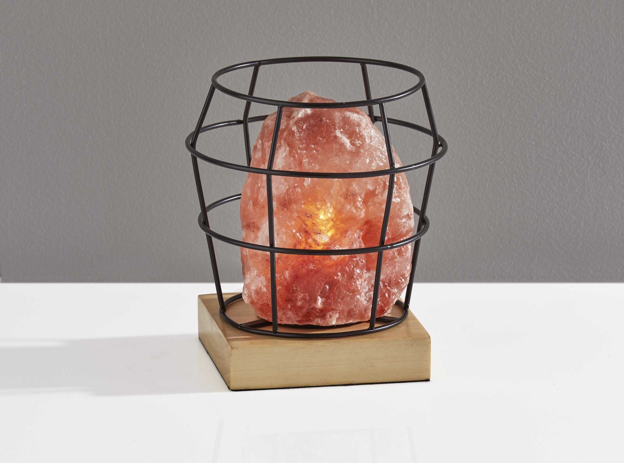 Himalayan salt table lamp with black wire basket and natural wood base, emitting a warm glow.