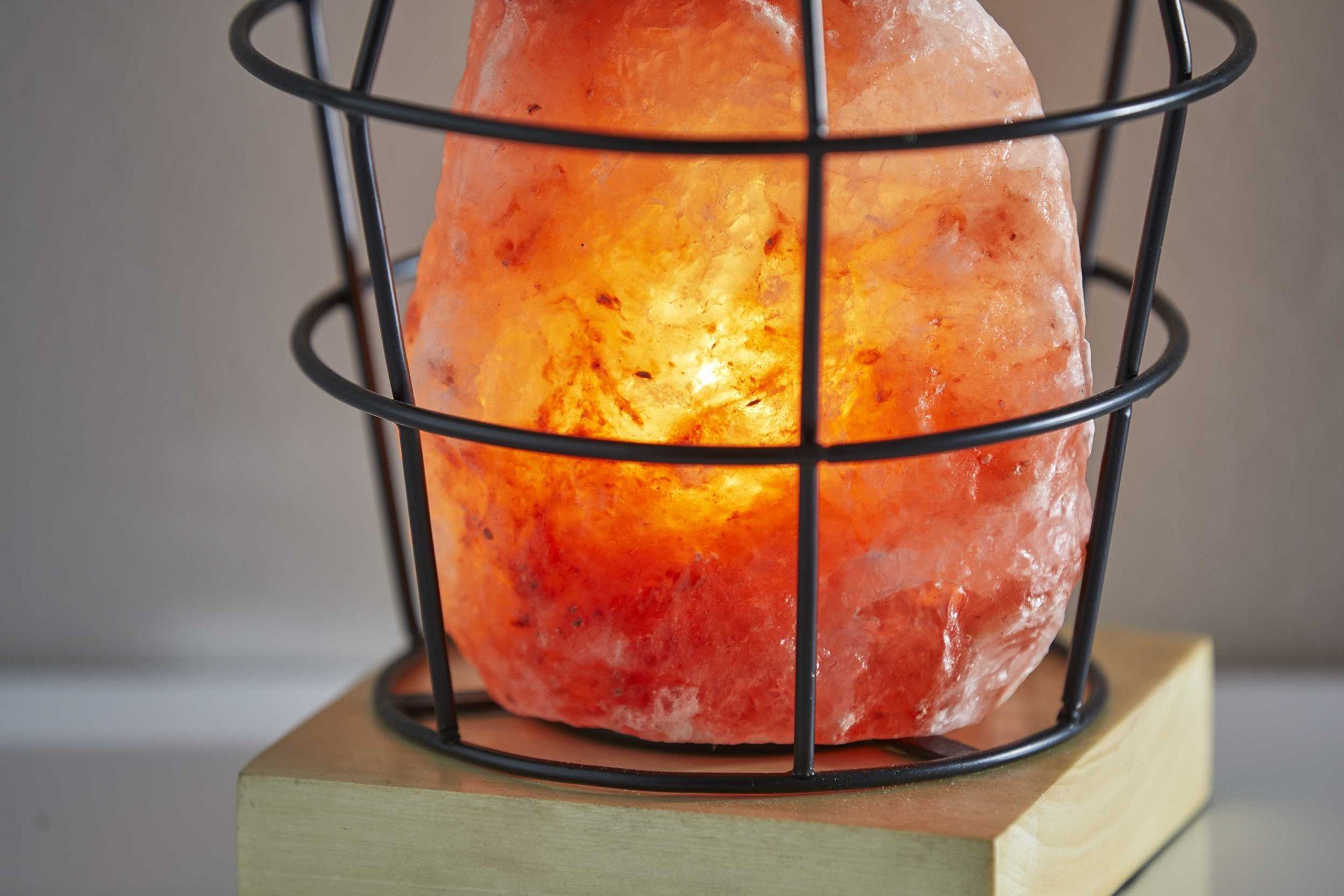 Himalayan salt table lamp with black wire basket and natural wood base, emitting a warm glow.