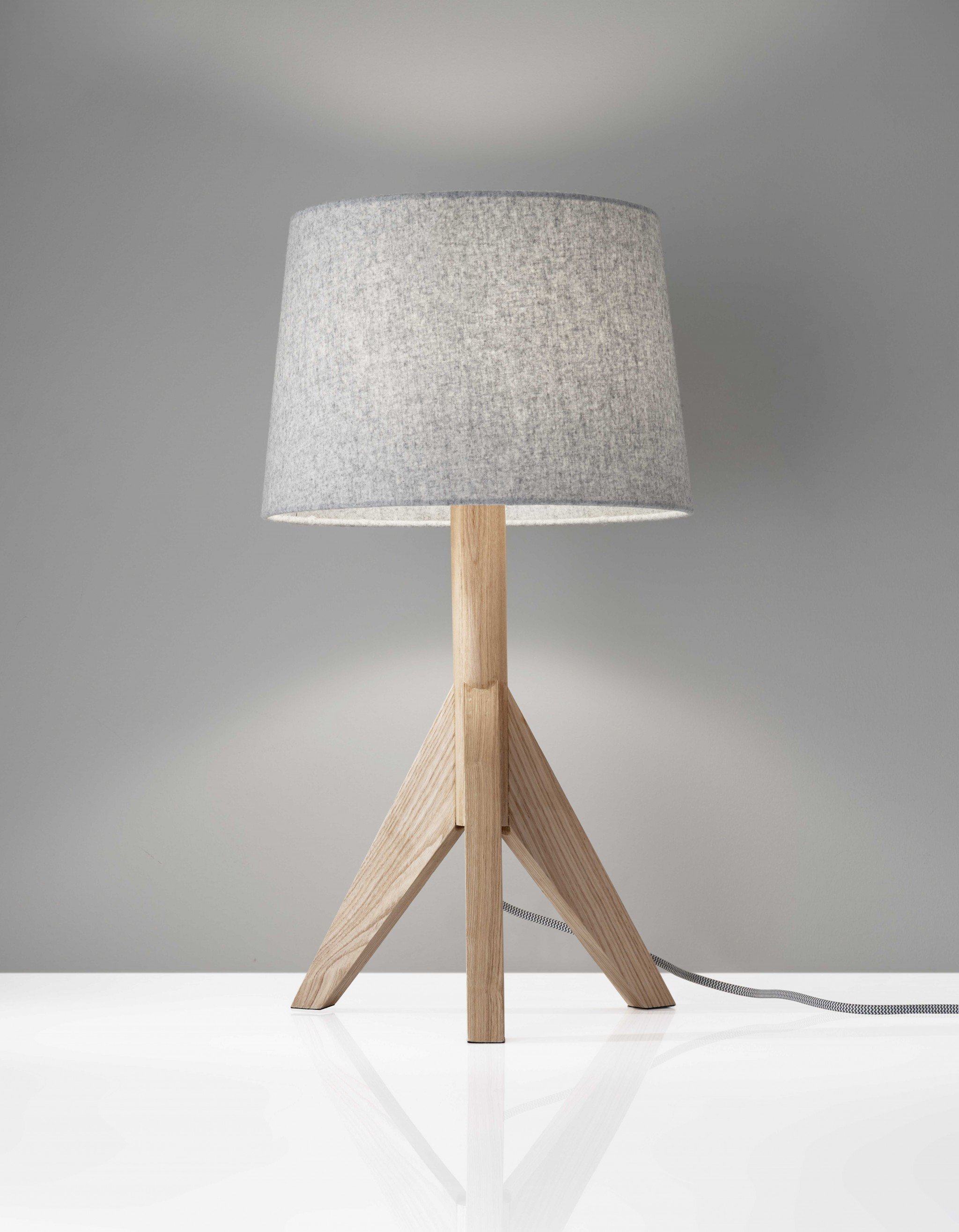 Natural wood tripod base table lamp with grey felt tapered drum shade, featuring a black and white fabric-covered cord.