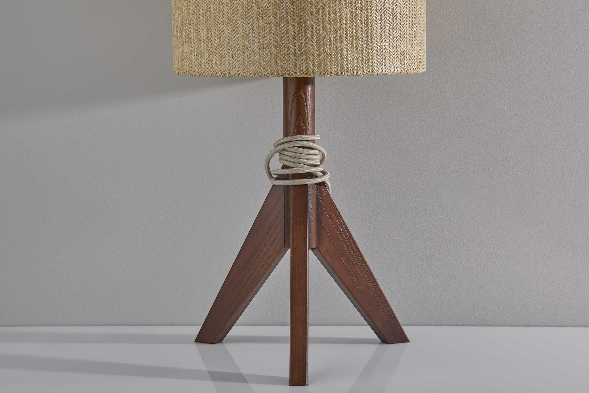 Natural wood tripod base table lamp with grey felt tapered drum shade, featuring a black and white fabric-covered cord.