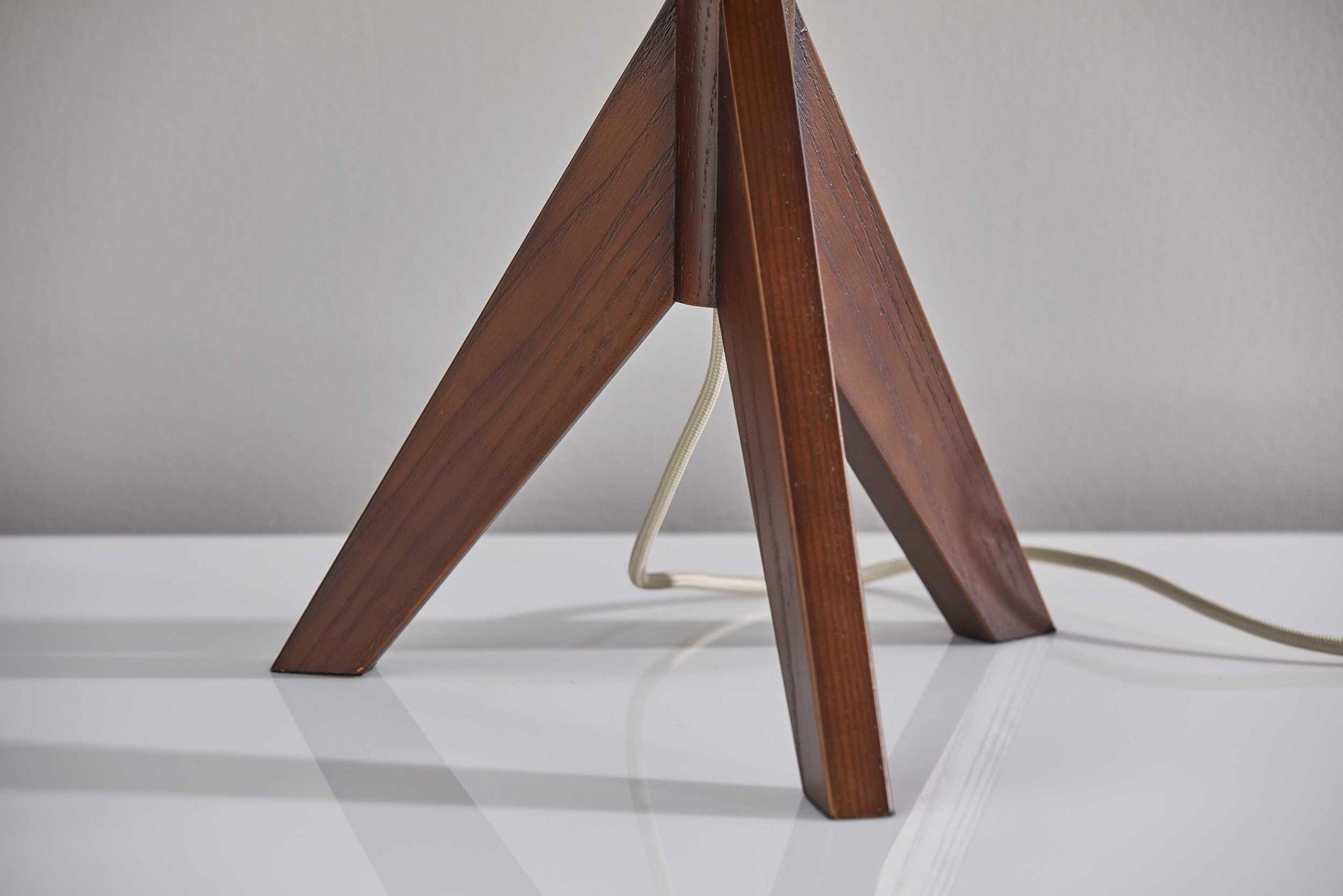 Natural wood tripod base table lamp with grey felt tapered drum shade, featuring a black and white fabric-covered cord.