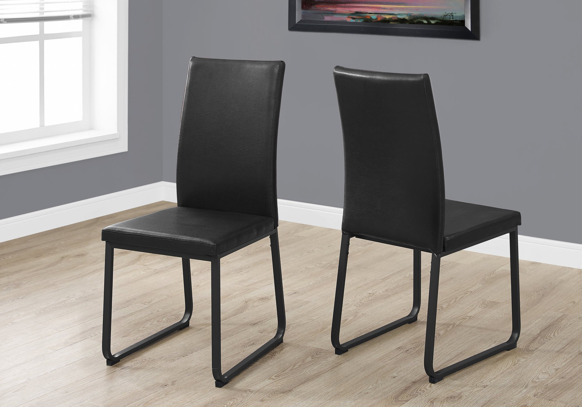 Two stylish black faux leather and metal dining chairs with foam padding, showcasing a modern design suitable for any dining space.