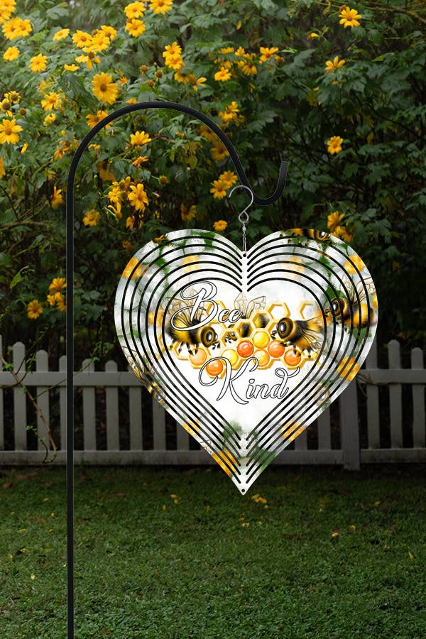 A colorful 10-inch double-sided heart-shaped wind spinner featuring a 'Be Kind' design, hanging from a hook in a garden setting.