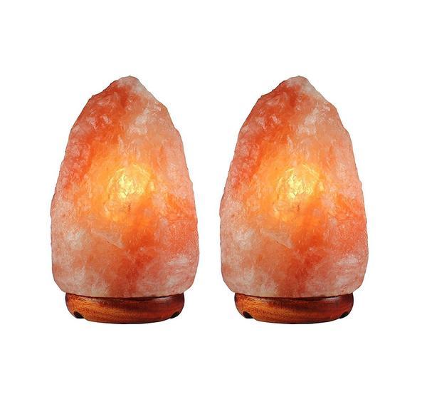 A pair of hand-carved Himalayan salt lamps with unique shapes, emitting a warm amber glow, placed on a wooden surface.