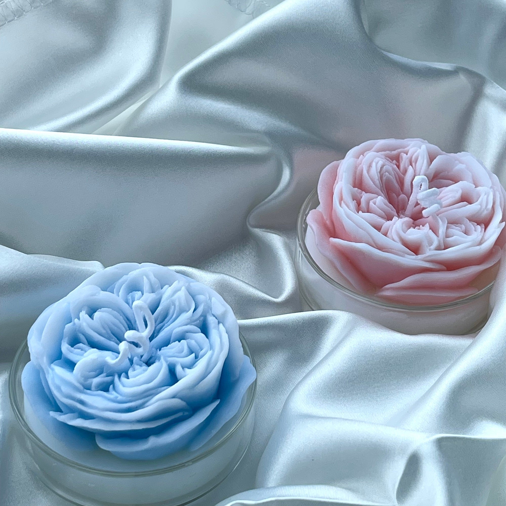 A beautifully arranged 2-Pack Rose Candle set featuring a pink rose candle and a blue rose candle in elegant glass containers.