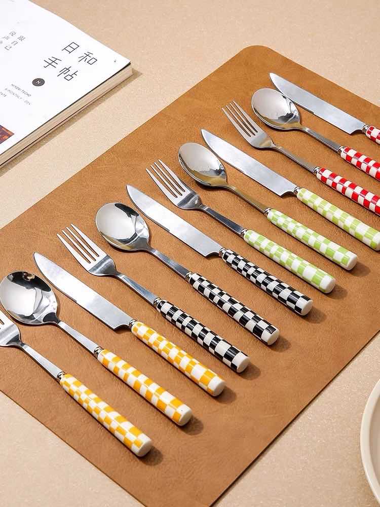 A vibrant 6-pack modern checkered flatware set featuring stainless steel utensils with colorful ceramic handles in red, yellow, green, and black.