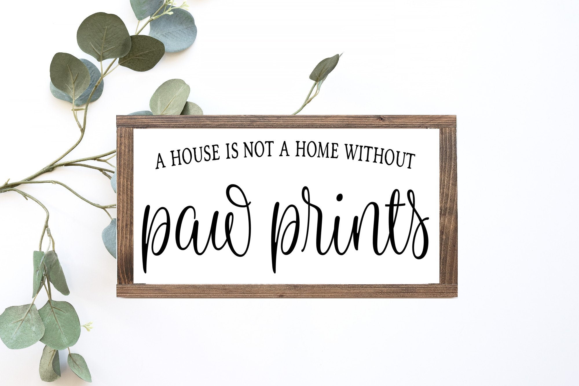 A rustic wood sign that reads 'A House Is Not A Home Without Paw Prints', featuring a matte white background and unique wood grain.