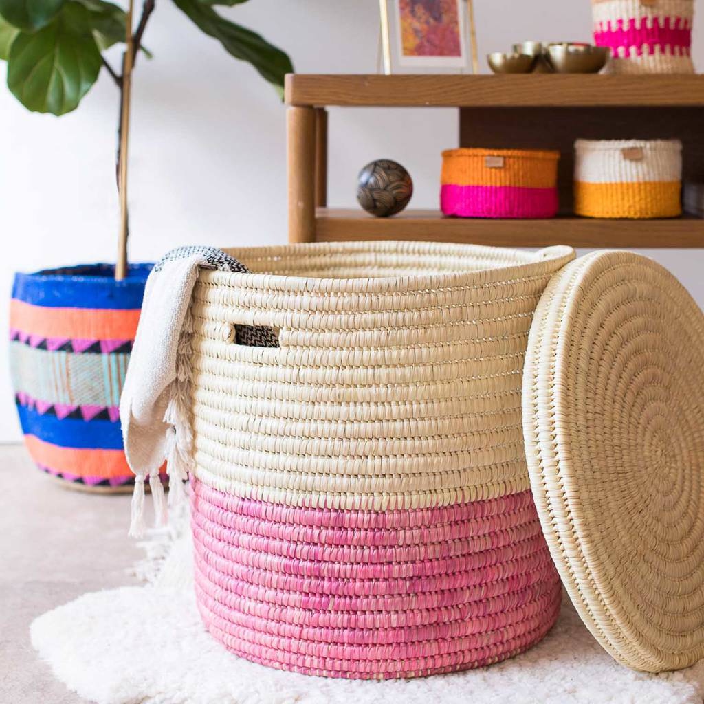 A vibrant African handcrafted laundry basket made from doum palm leaf, featuring a raspberry pink color block design, showcasing its lidded structure and unique craftsmanship.