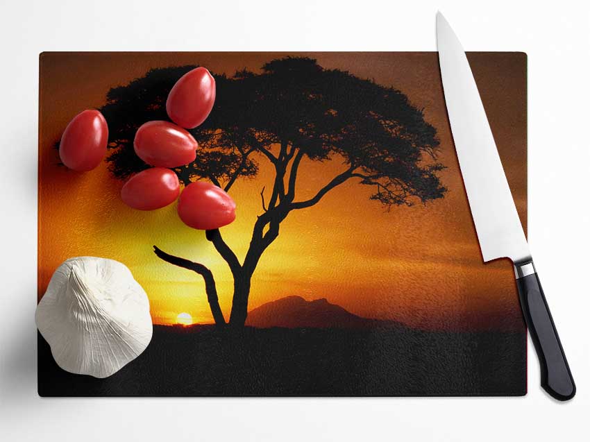 A beautifully designed chopping board featuring an African tree silhouette in golden sunlight, made from durable tempered glass.