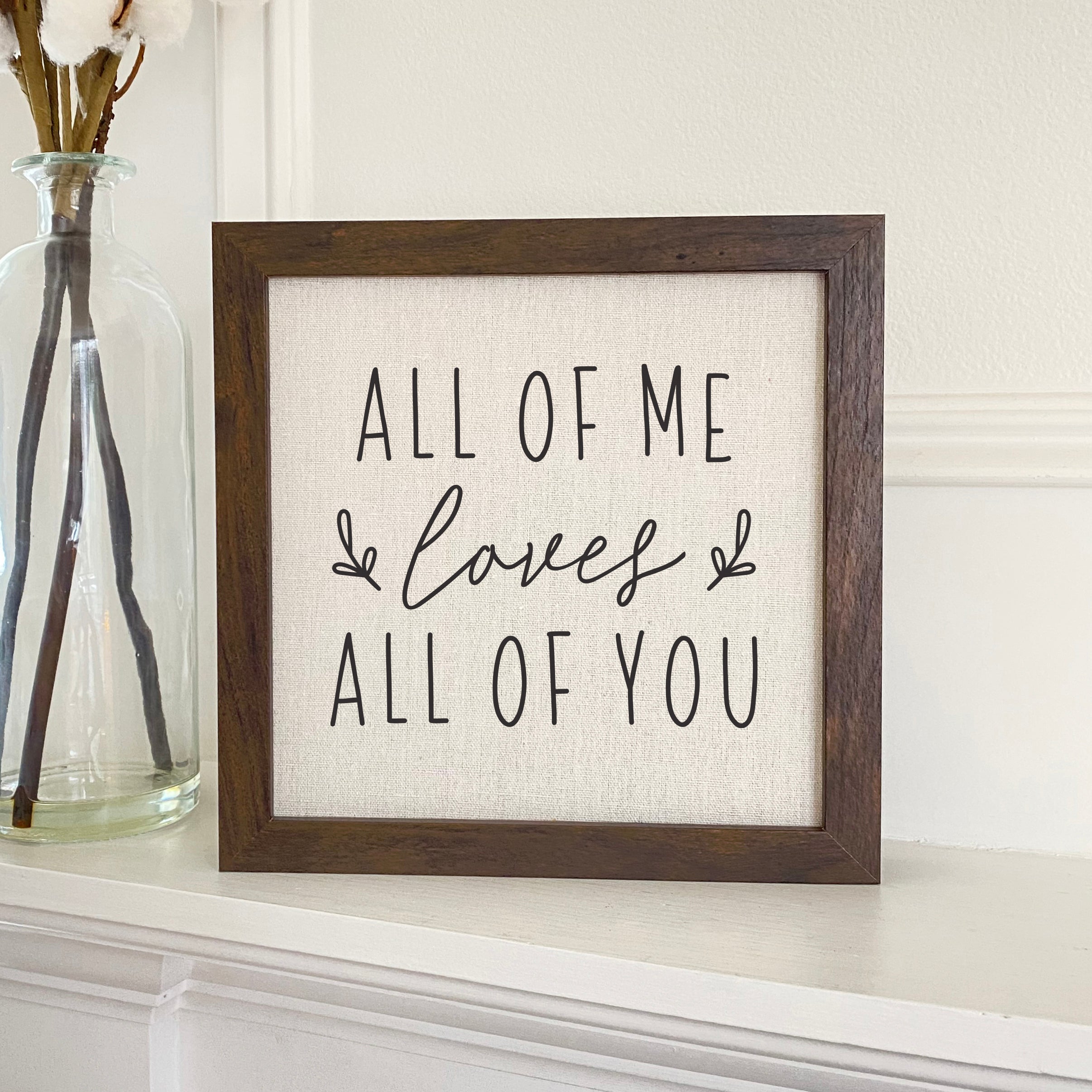 Framed sign with the text 'All of Me Loves All of You' in a stylish wood frame, featuring a linen-look background.