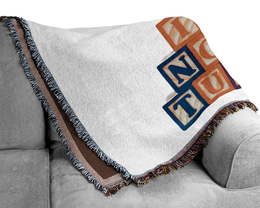 A soft pink blanket featuring alphabet blocks design, made from 100% cotton, draped elegantly on a couch.