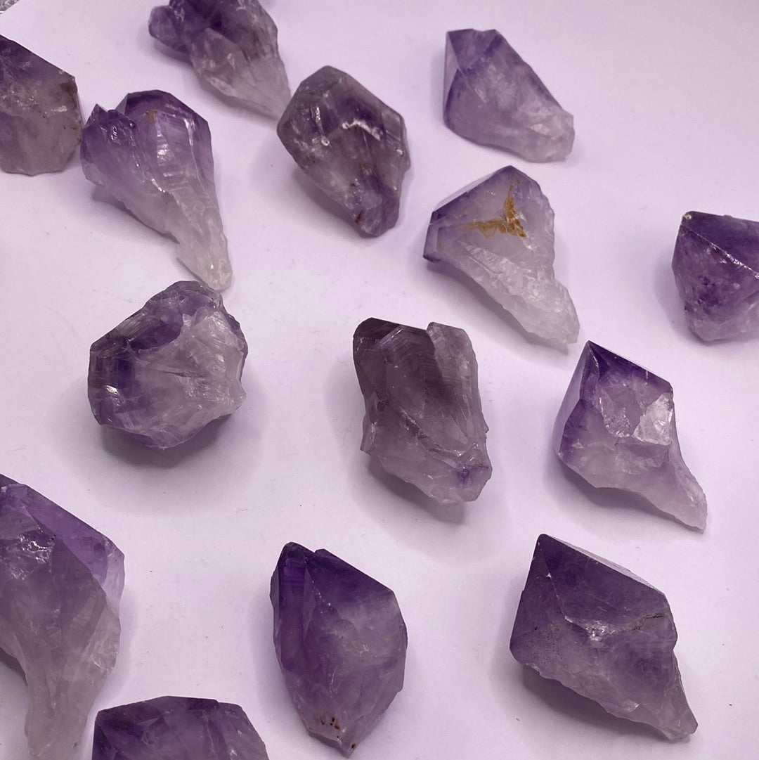 A collection of Amethyst Natural Points showcasing various shades of purple, each uniquely shaped and tumbled, reflecting light beautifully.