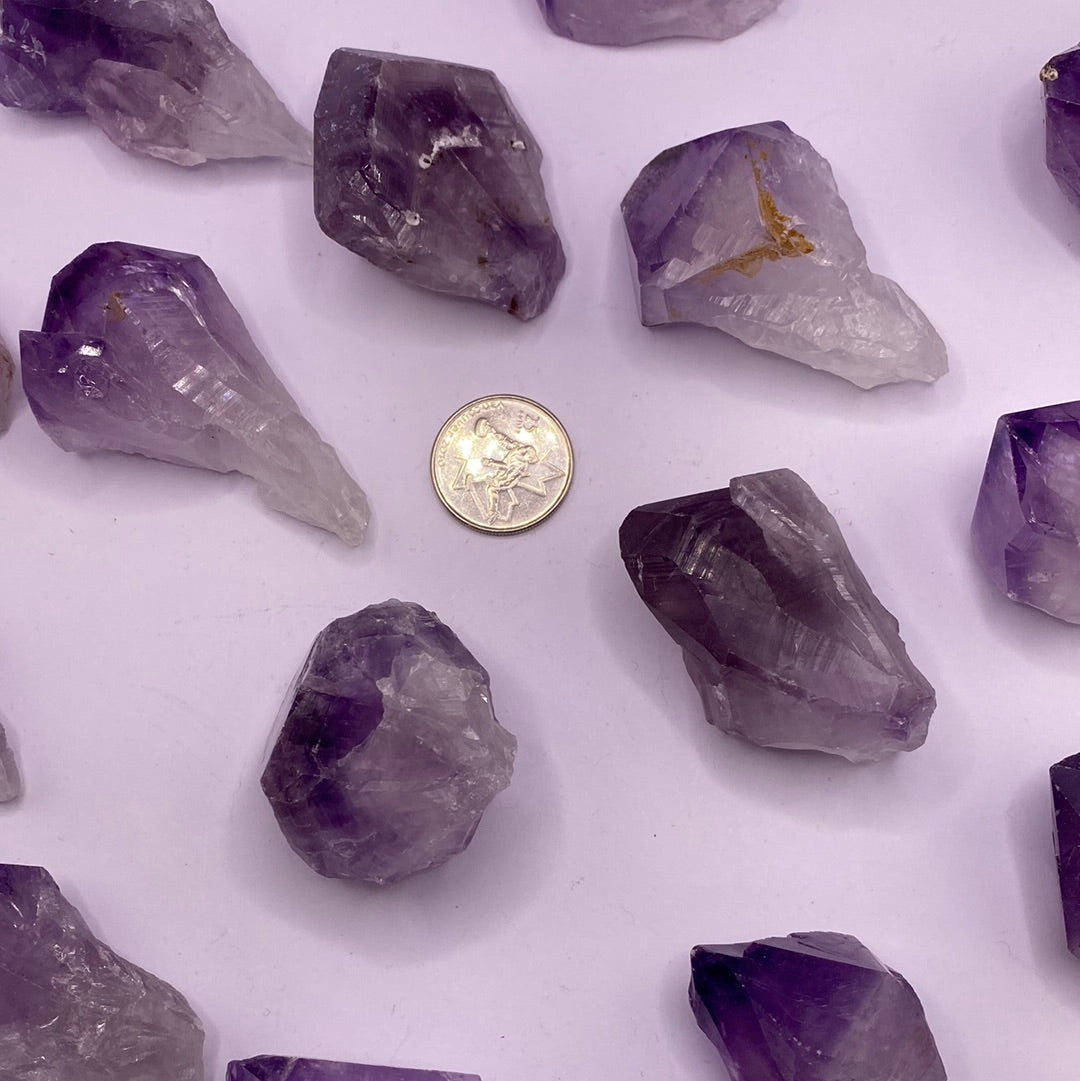 A collection of Amethyst Natural Points showcasing various shades of purple, each uniquely shaped and tumbled, reflecting light beautifully.