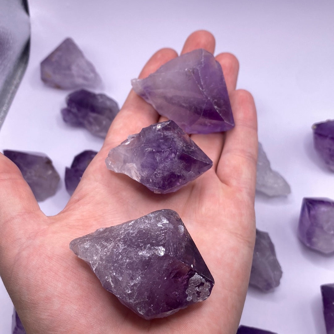 A collection of Amethyst Natural Points showcasing various shades of purple, each uniquely shaped and tumbled, reflecting light beautifully.