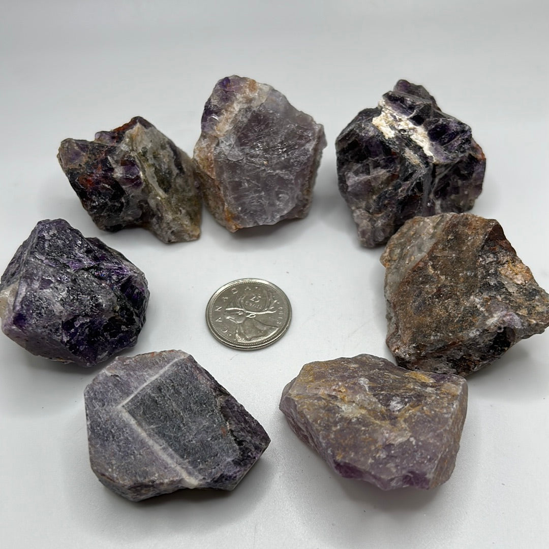 A collection of rough cut Amethyst stones, showcasing their natural purple hues and unique textures, approximately 1-2 inches in size.