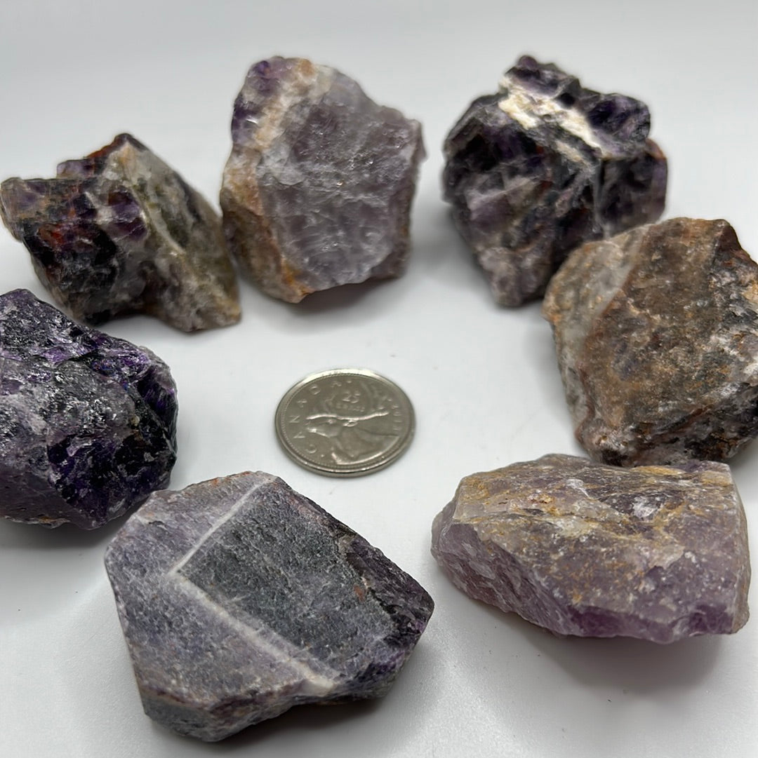 A collection of rough cut Amethyst stones, showcasing their natural purple hues and unique textures, approximately 1-2 inches in size.