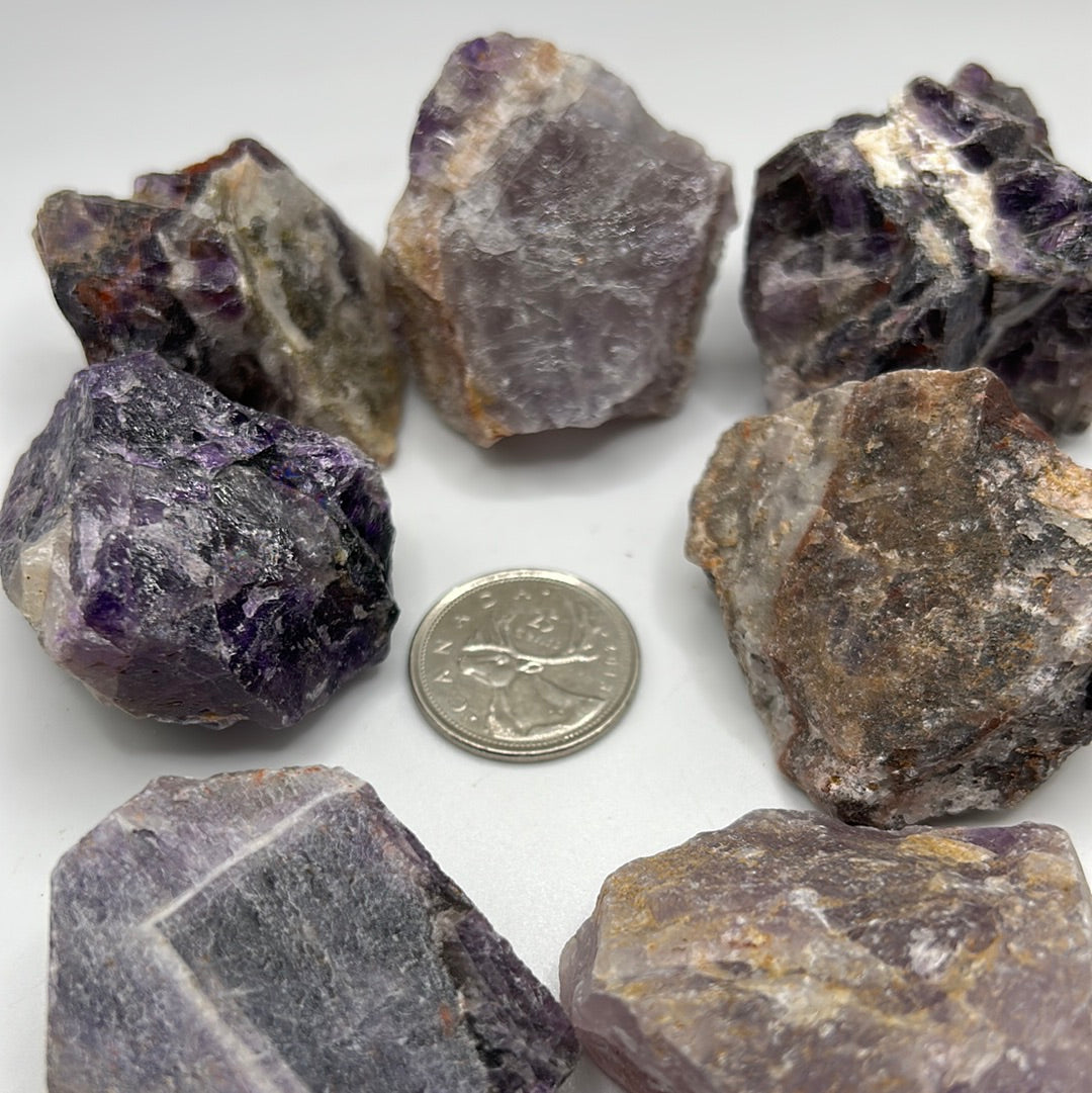 A collection of rough cut Amethyst stones, showcasing their natural purple hues and unique textures, approximately 1-2 inches in size.