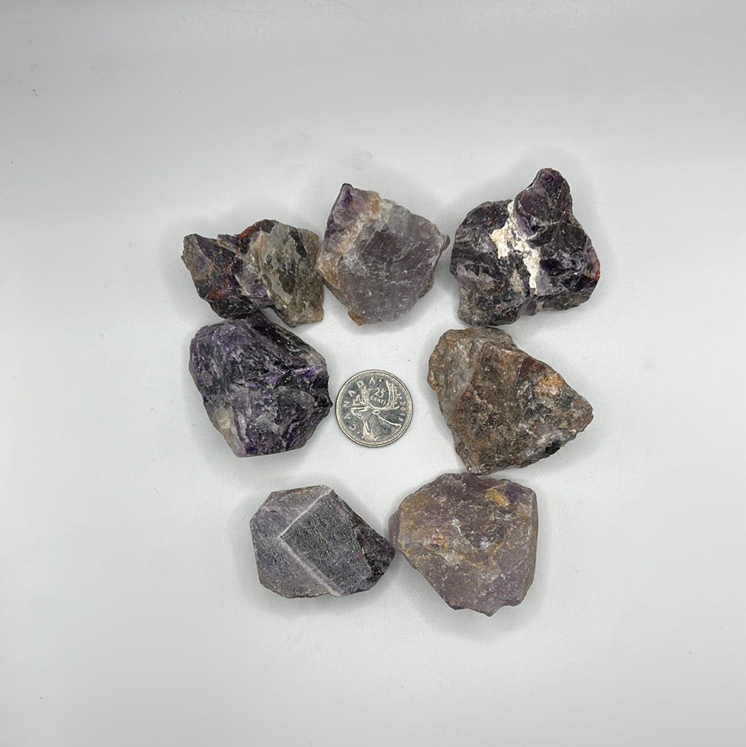 A collection of rough cut Amethyst stones, showcasing their natural purple hues and unique textures, approximately 1-2 inches in size.