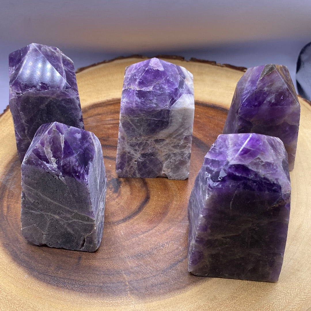 A polished Amethyst crystal point with a smooth purple surface and a natural raw bottom, showcasing its beauty and healing properties.