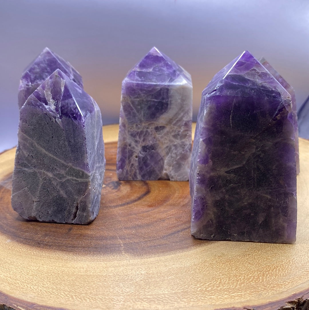 A polished Amethyst crystal point with a smooth purple surface and a natural raw bottom, showcasing its beauty and healing properties.