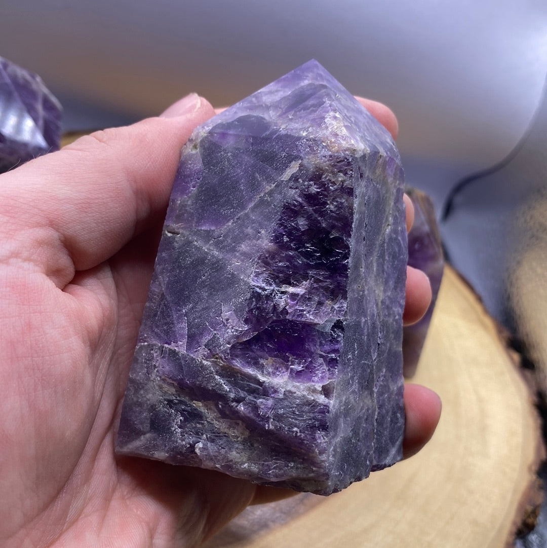 A polished Amethyst crystal point with a smooth purple surface and a natural raw bottom, showcasing its beauty and healing properties.