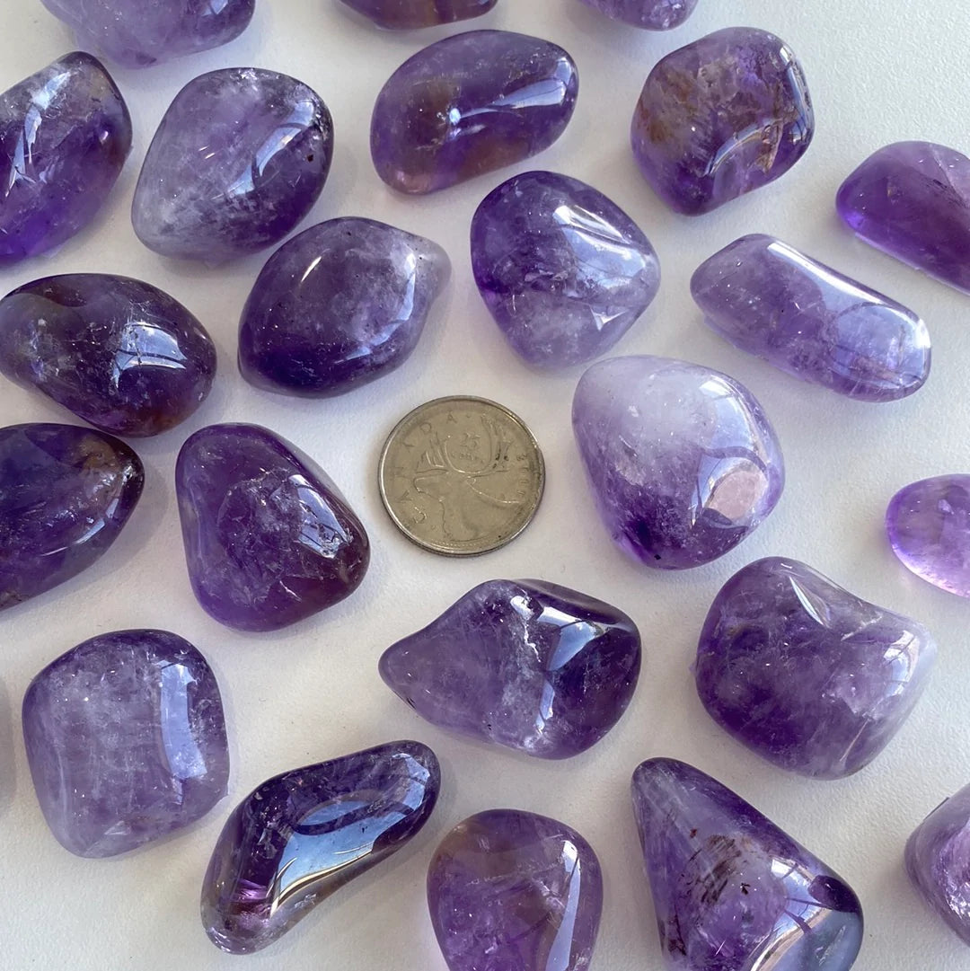 A collection of polished amethyst tumbled stones showcasing various shades of purple, from light lavender to deep violet, each with unique shapes.