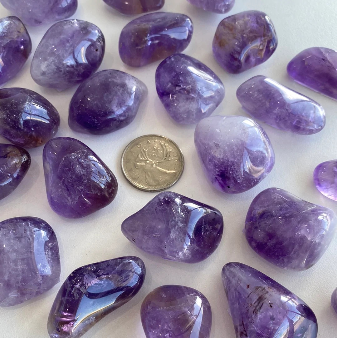 A collection of polished amethyst tumbled stones showcasing various shades of purple, from light lavender to deep violet, each with unique shapes.