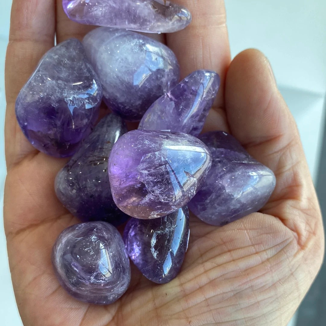 A collection of polished amethyst tumbled stones showcasing various shades of purple, from light lavender to deep violet, each with unique shapes.