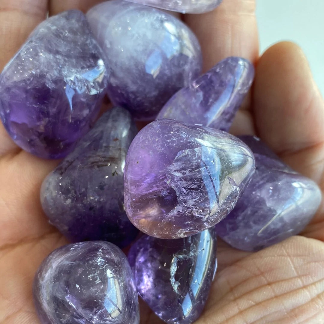 A collection of polished amethyst tumbled stones showcasing various shades of purple, from light lavender to deep violet, each with unique shapes.