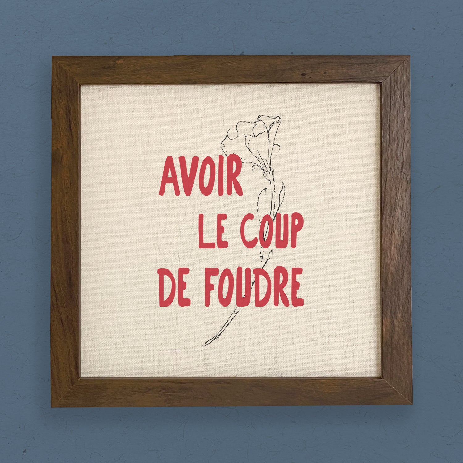 A stylish framed sign reading 'Avoir le Coup de Foudre' with a natural wood frame, perfect for home decor.