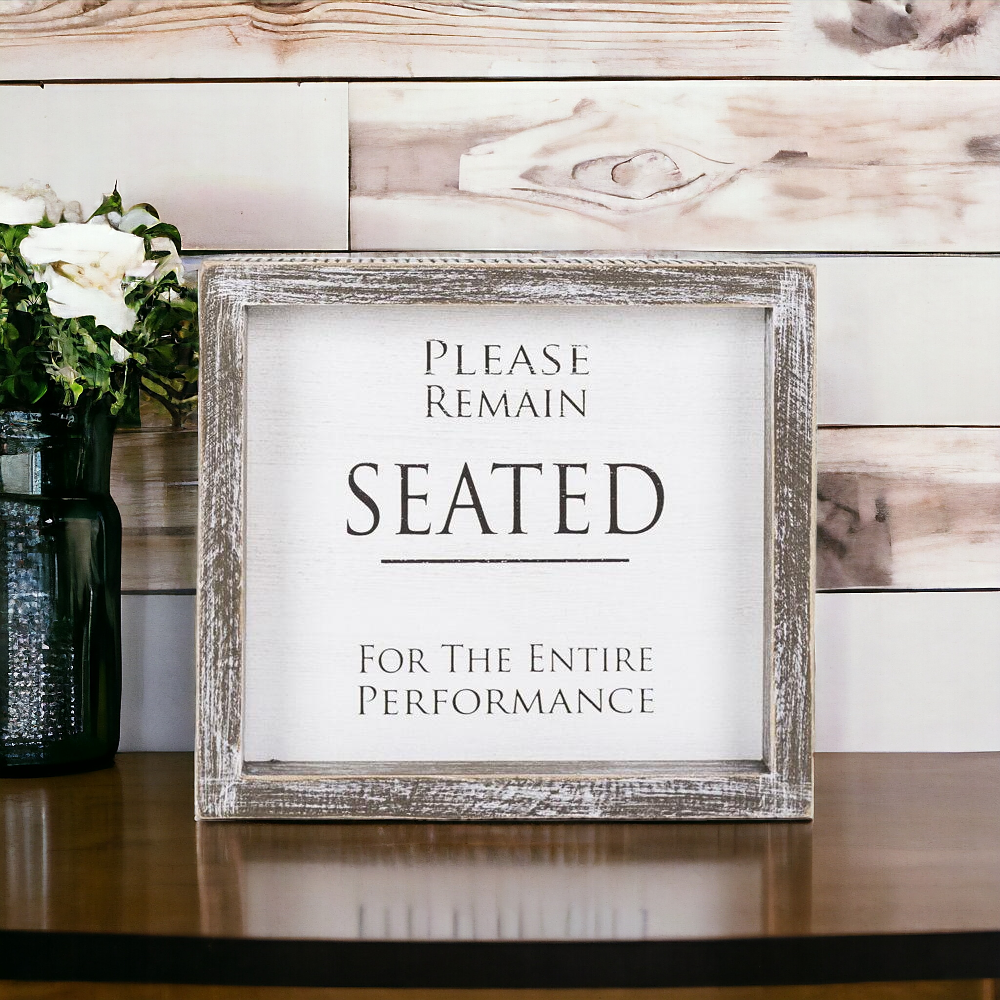 A versatile wood sign displaying 'Please Remain Seated For The Entire Performance' in black and white, suitable for bathrooms and theaters.