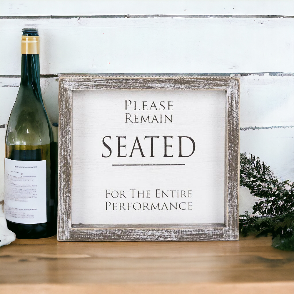 A versatile wood sign displaying 'Please Remain Seated For The Entire Performance' in black and white, suitable for bathrooms and theaters.