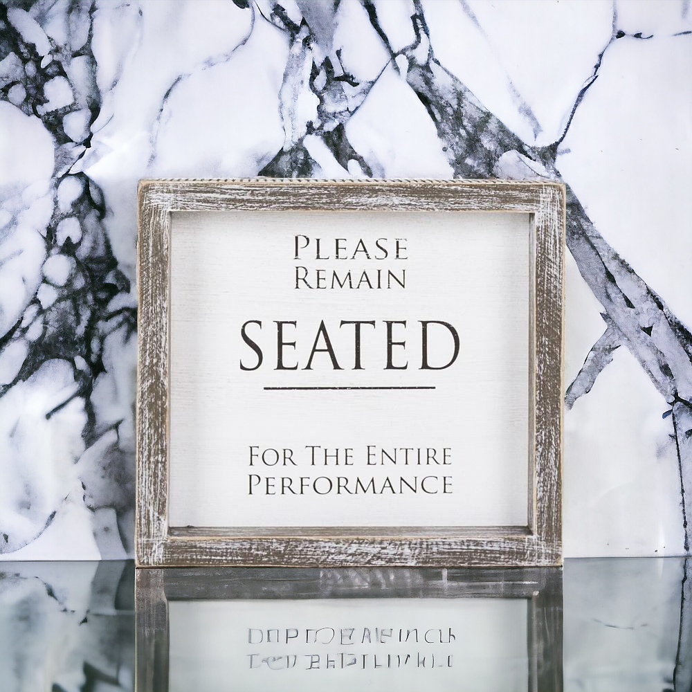 A versatile wood sign displaying 'Please Remain Seated For The Entire Performance' in black and white, suitable for bathrooms and theaters.