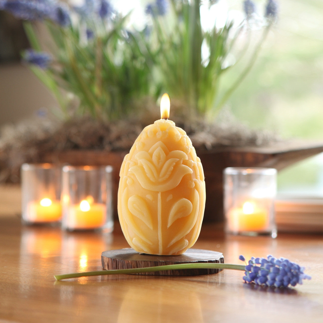 A beautifully crafted 3.5-inch tall beeswax egg pillar candle with an intricate floral design, glowing softly.