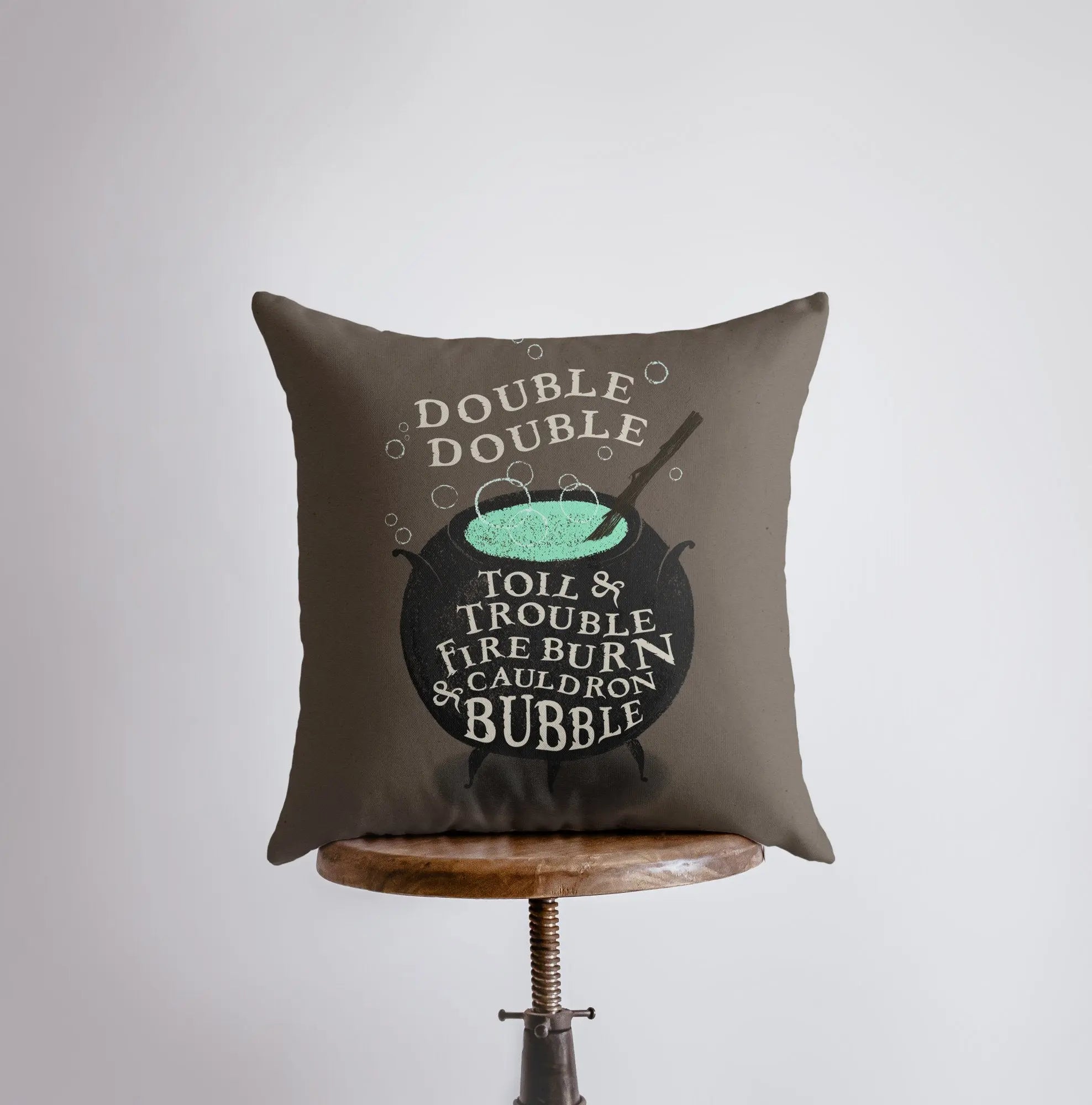 Black Cauldron Boiling Pillow Cover featuring a spooky cauldron design on a taupe background with Halloween-themed text.