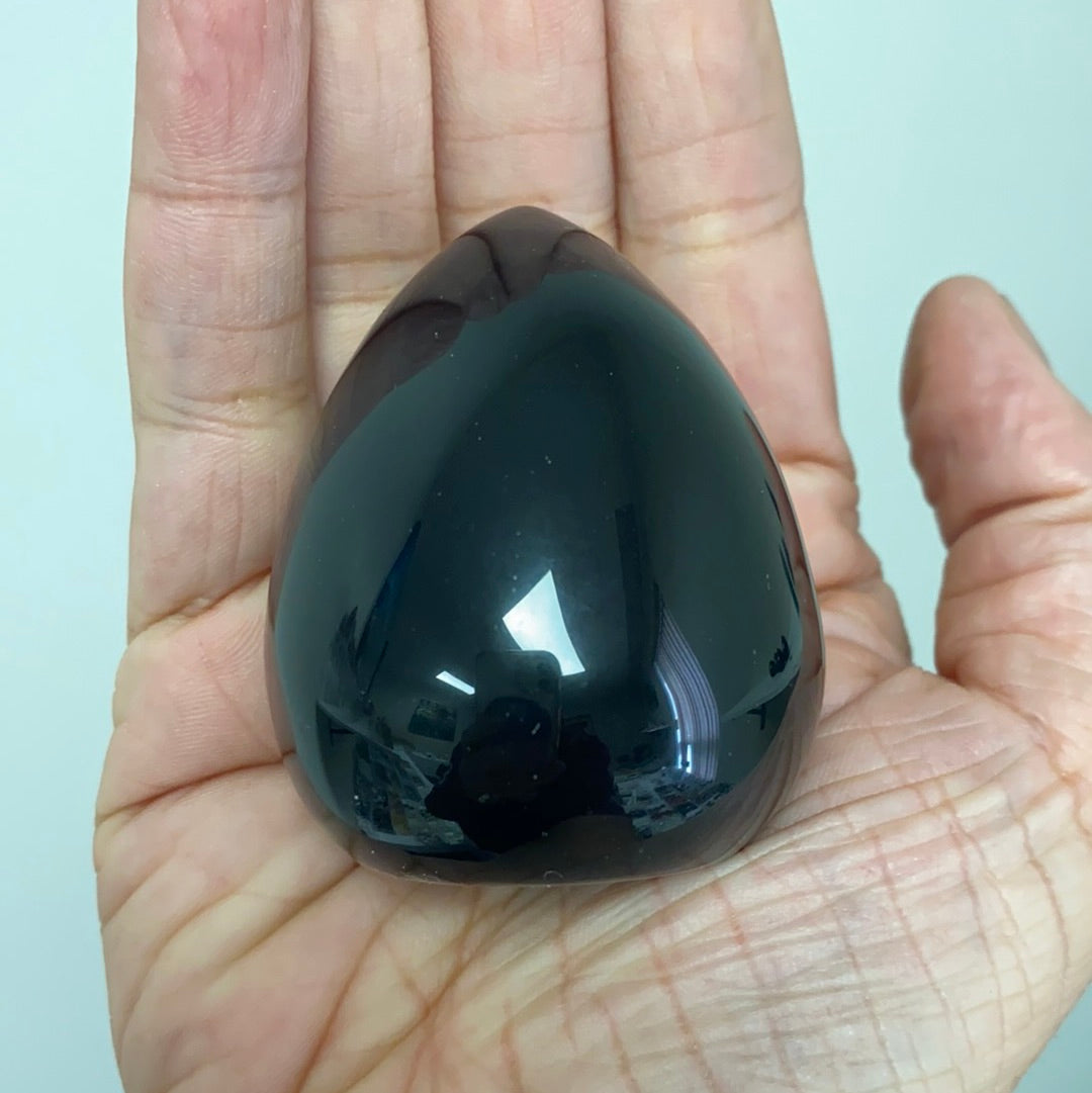 A polished Black Obsidian Cut Base Egg, showcasing its glossy surface and deep black color, standing 2.5 inches tall.